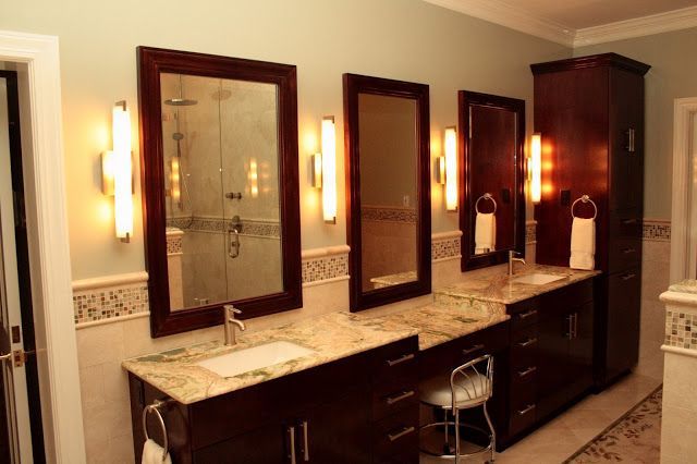 Bathroom with three mirrors, vanity, dark cabinets, granite countertops, and sconce lighting.