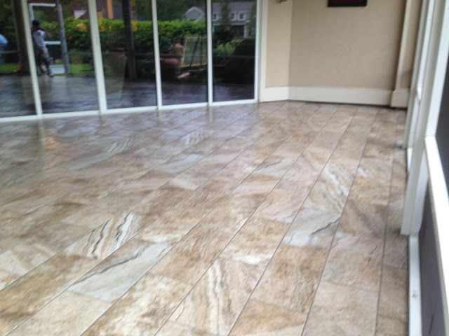 Tiled outdoor patio with a glossy, stone-like appearance. Large glass windows and beige walls in the background.
