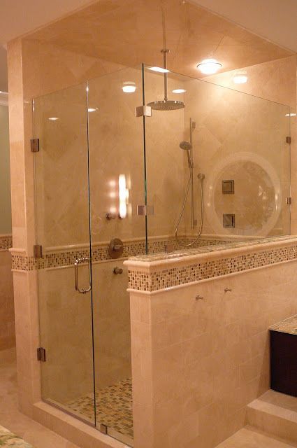 Glass-enclosed shower in beige-toned bathroom, featuring a rain showerhead, hand shower, and tiled walls with a mosaic border.