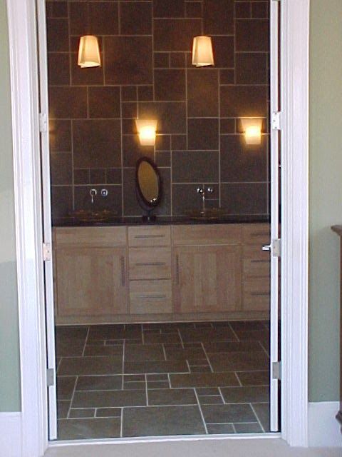 Bathroom interior: wooden vanity, dark tiled walls/floor, sconce lighting, oval mirror.