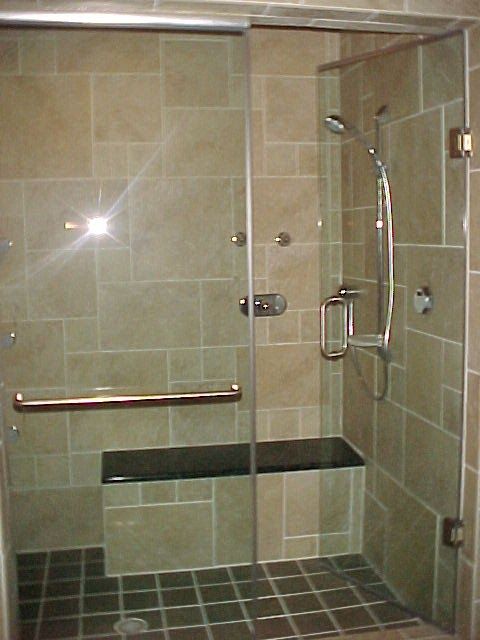 Shower with glass doors, stone tile walls and floor, built-in bench, and chrome fixtures.
