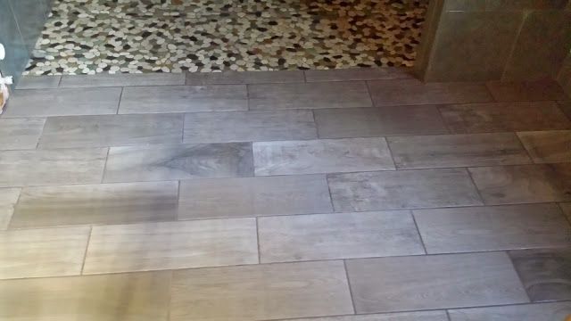 Gray rectangular floor tiles in a bathroom, transitioning to pebble-style shower floor.