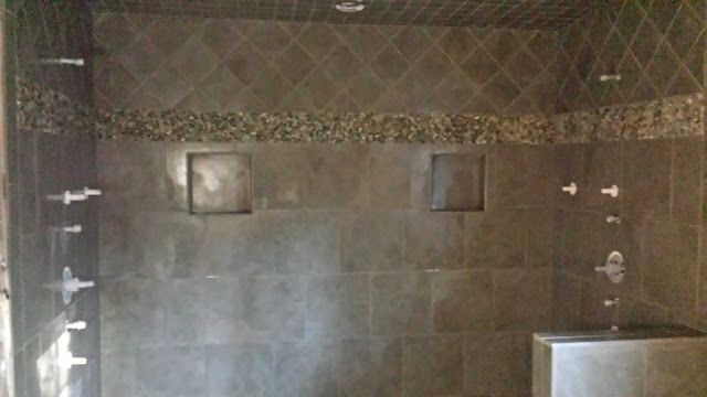 Brown tiled shower with recessed shelves, pebble accent, and multiple shower heads.