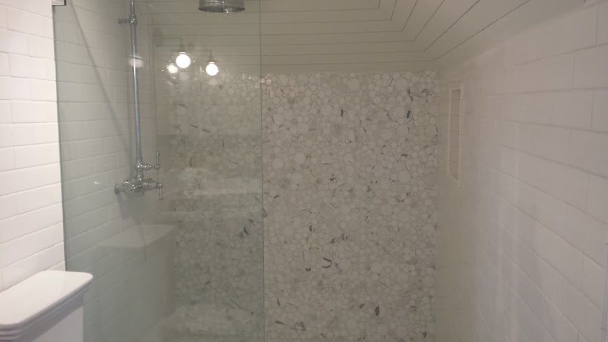 Shower with glass door, white tiled walls, and textured accent wall. Silver showerhead and fixtures visible.