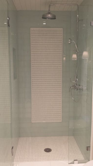 Shower with glass doors, white tiled walls and floor, and silver fixtures.