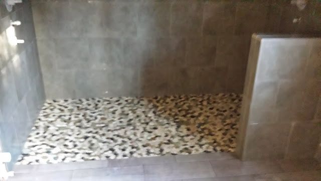 Shower stall with stone tile floor and gray tile walls.