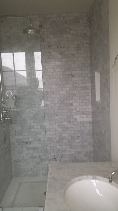 Bathroom shower with marble tile walls and glass door. White oval sink is visible.