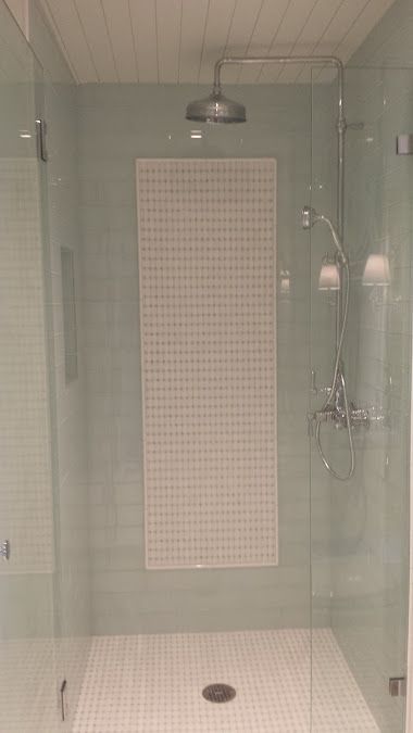 Shower with glass doors and a white tile design on the back wall.