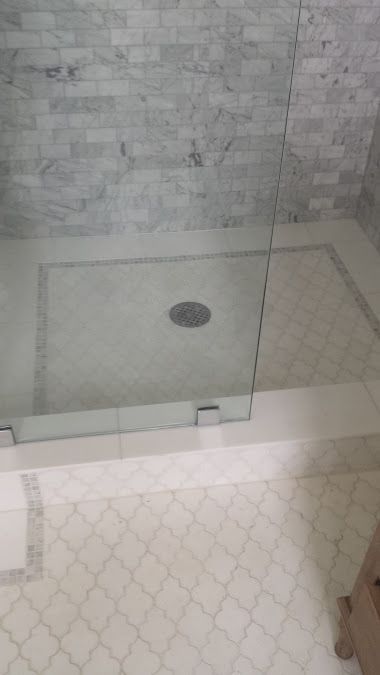 Marble shower with glass door. White tile floor with decorative accents.