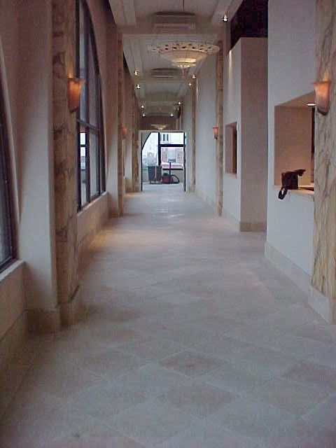 Long hallway with arched windows, light-colored walls and floor, and decorative pillars.