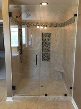 Glass shower enclosure with beige tiled walls, mosaic tile accents, and dark hardware.