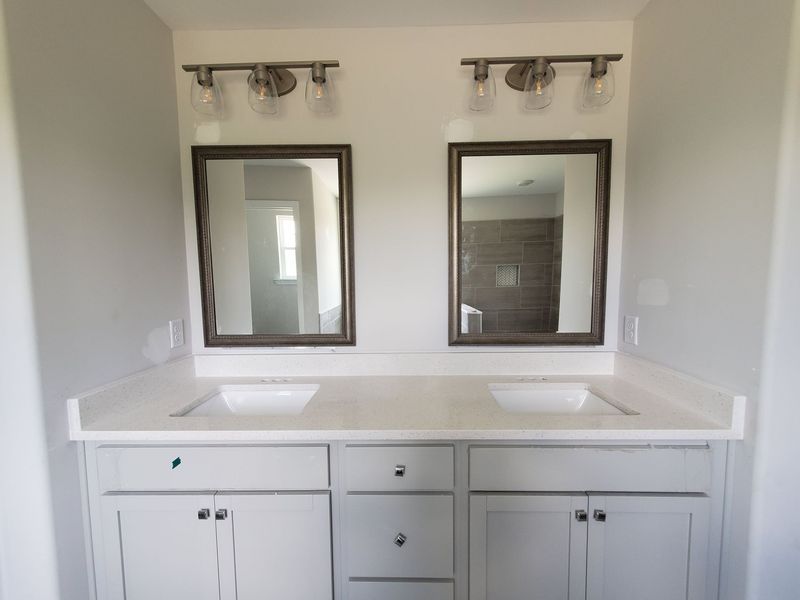 Two-sink bathroom vanity with gray cabinets, white countertop, and framed mirrors; light fixtures above.