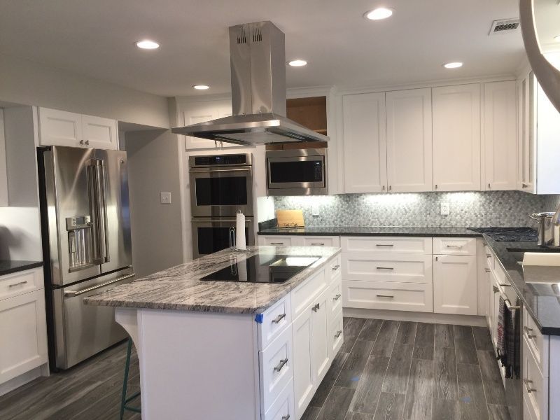 Modern white kitchen with stainless steel appliances, island, and wood-look flooring.