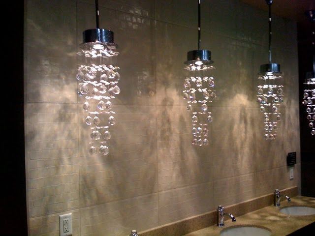 Three hanging crystal pendant lights above bathroom sinks, casting patterned shadows on a beige tiled wall.
