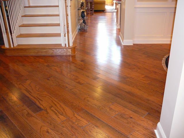 Hardwood floor hallway with stairs on the left. Shiny, medium-brown floor reflects light. White trim.