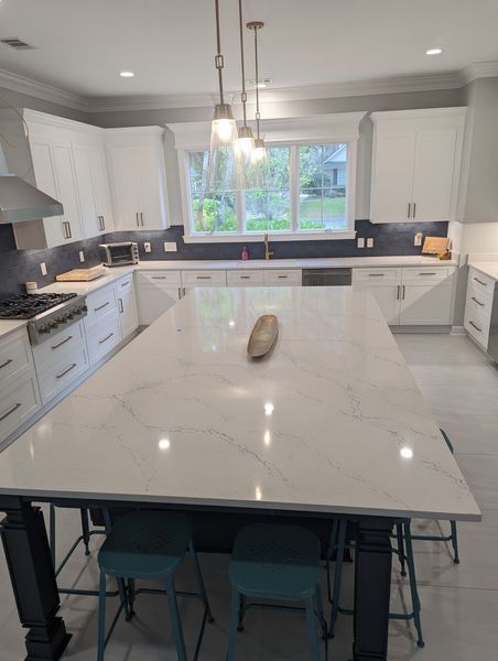 Modern white kitchen with a large island, pendant lights, and teal stools.