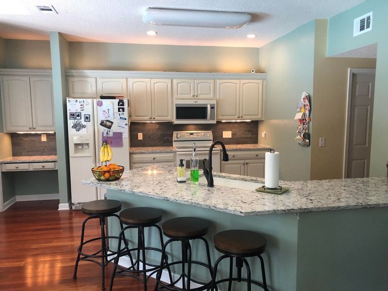 Kitchen with island, light cabinets, granite countertops, and wood floors. Bar stools at the island.