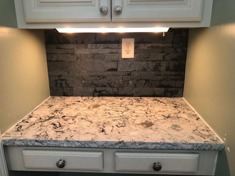 Kitchen countertop with dark gray stone backsplash, cream cabinets, and under-cabinet lighting.
