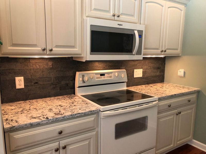 Kitchen with white cabinets, speckled countertops, black backsplash, and a white oven and microwave.