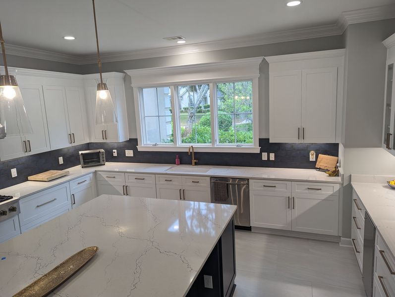 White kitchen with island, cabinets, and stainless steel appliances. Bright, modern design with a window.