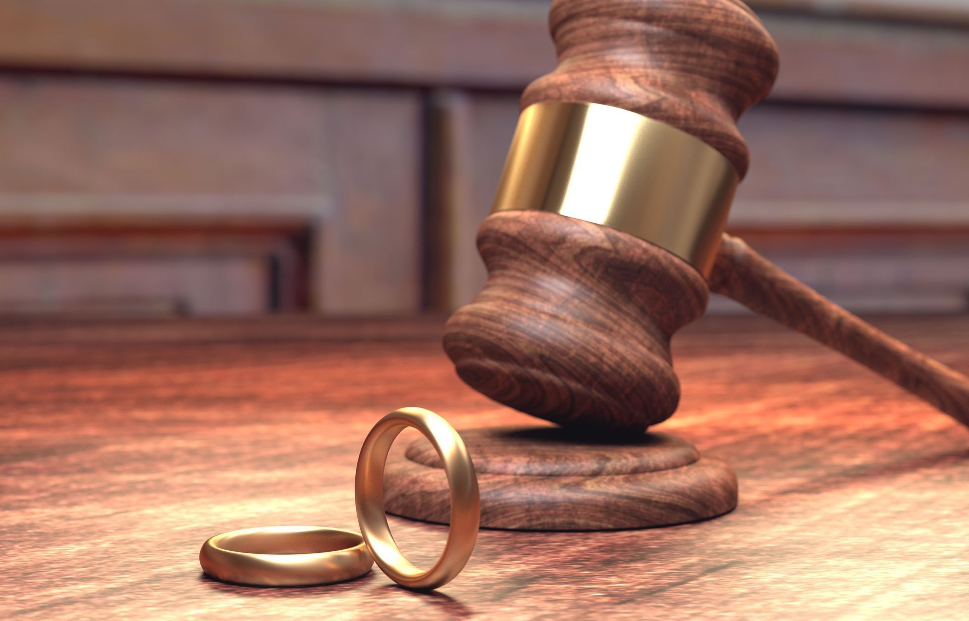 A wooden judge 's gavel and two wedding rings on a wooden table.