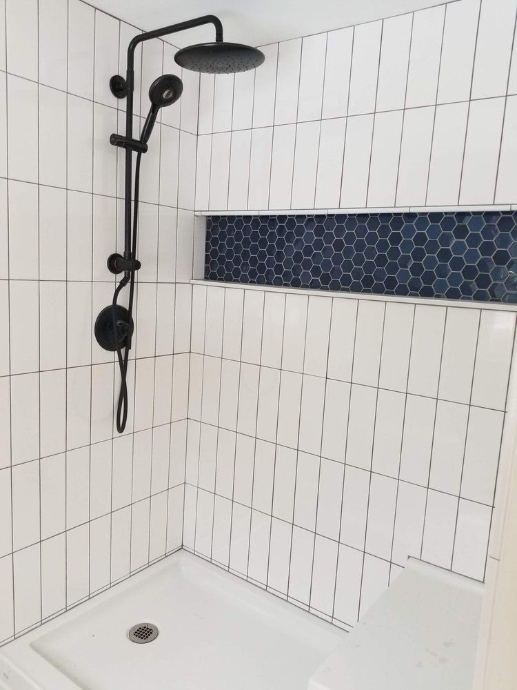A shower with white tiles and a black shower head.