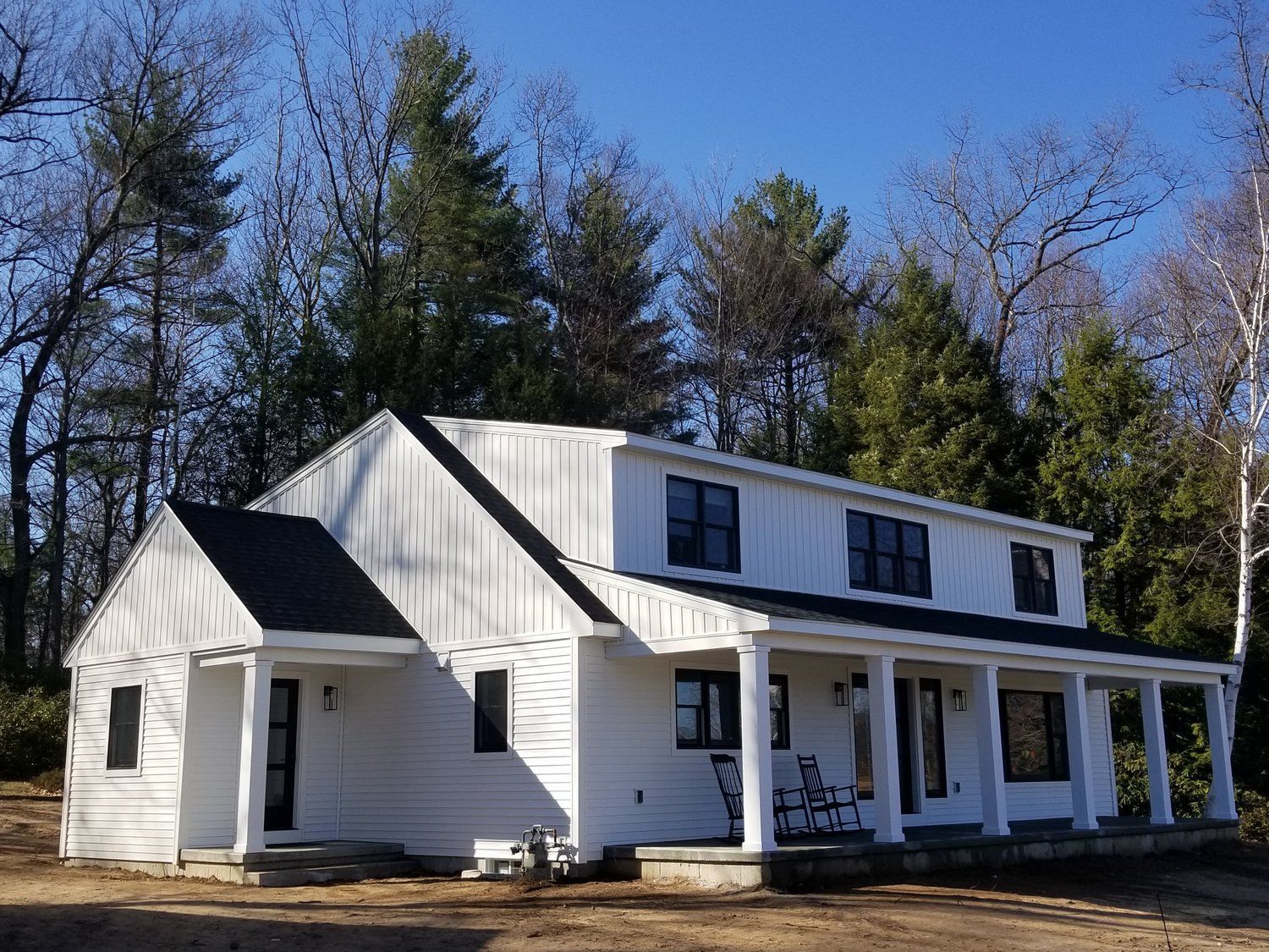 A white house with a black roof is surrounded by trees.