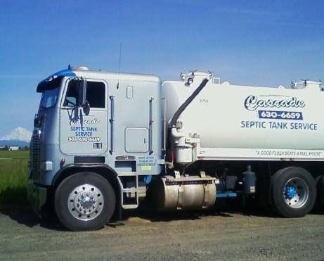 A white septic tank service truck is parked in a field