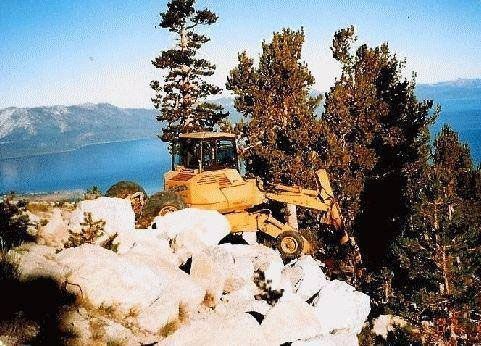 A bulldozer is clearing snow from a hillside near a lake