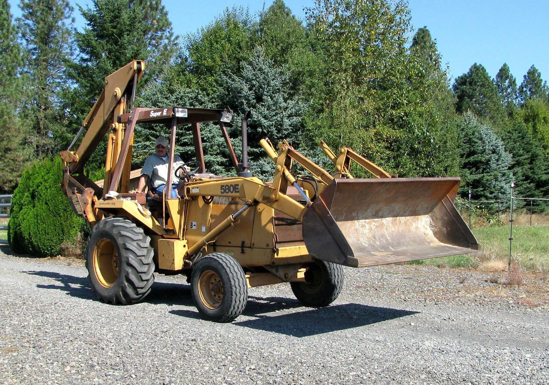 A man is driving a yellow tractor in a gravel driveway