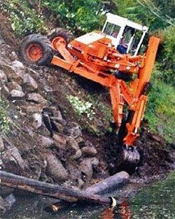 A bulldozer is driving down a rocky hill next to a body of water.