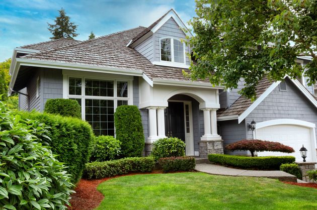 Suburban house with gray roof, white trim, manicured lawn, and attached garage surrounded by green trees