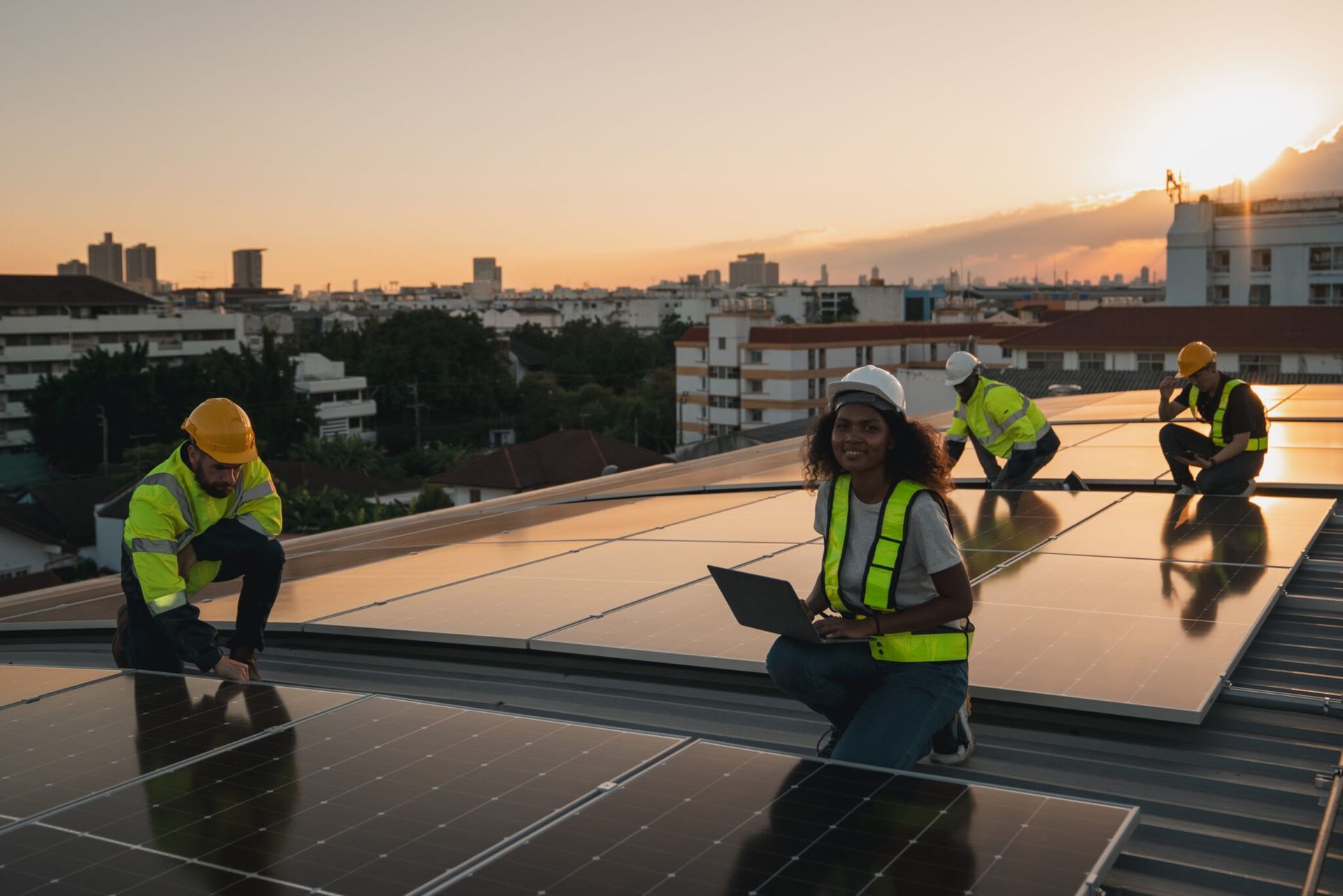 Workers installing solar panels on a rooftop at sunset, with a city skyline in the background
