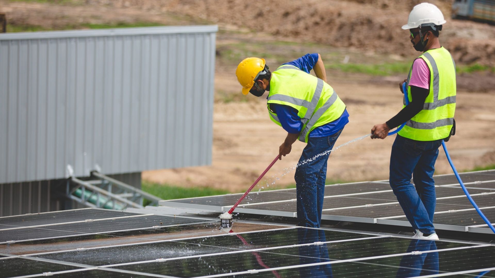 Construction workers in hard hats and safety vests installing roofing on a building site