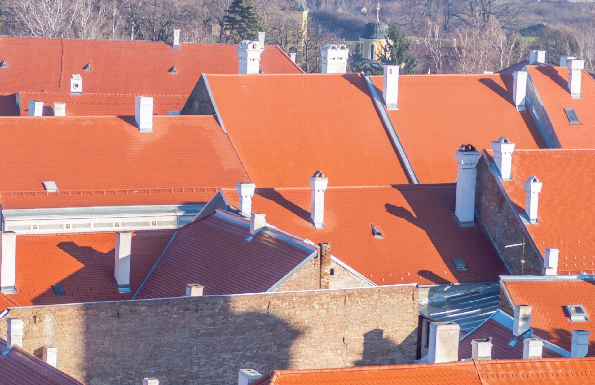 Rooftops with bright red tiles and chimneys in a dense residential neighborhood under daylight