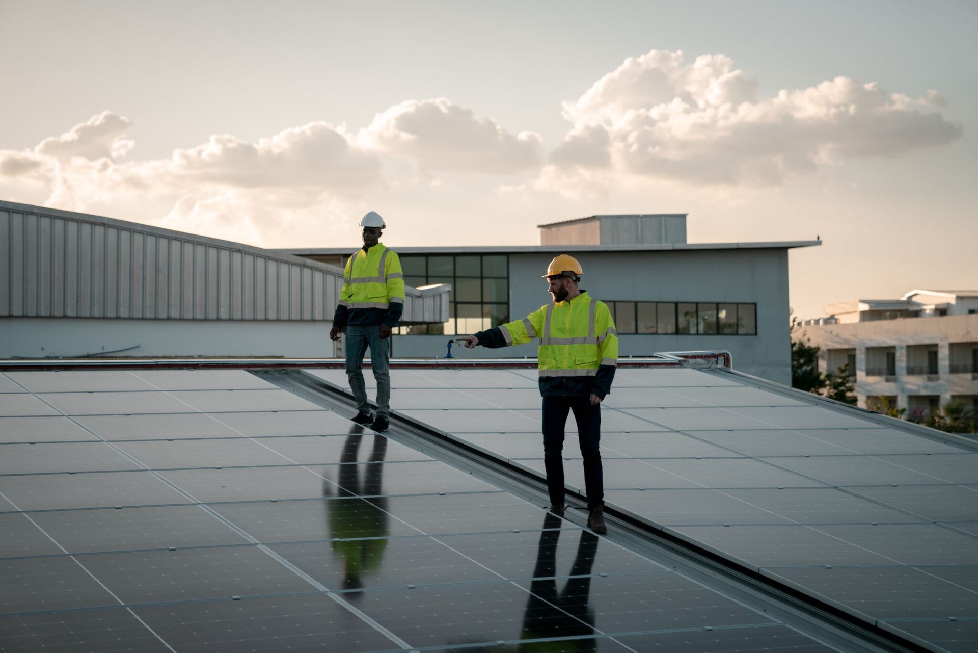Two workers in safety gear inspecting solar panels on a rooftop at sunset.