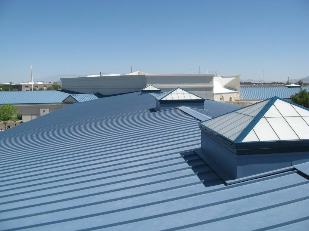 Blue corrugated metal rooftop with skylights overlooking water under a clear sky