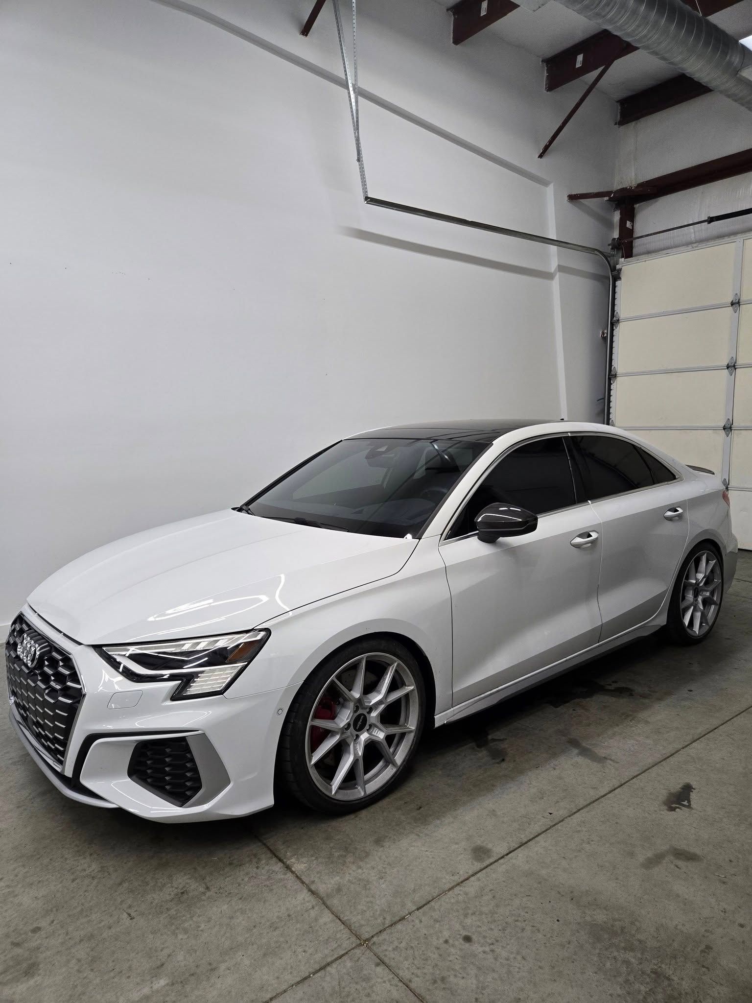 A white car is parked in a garage next to a garage door.