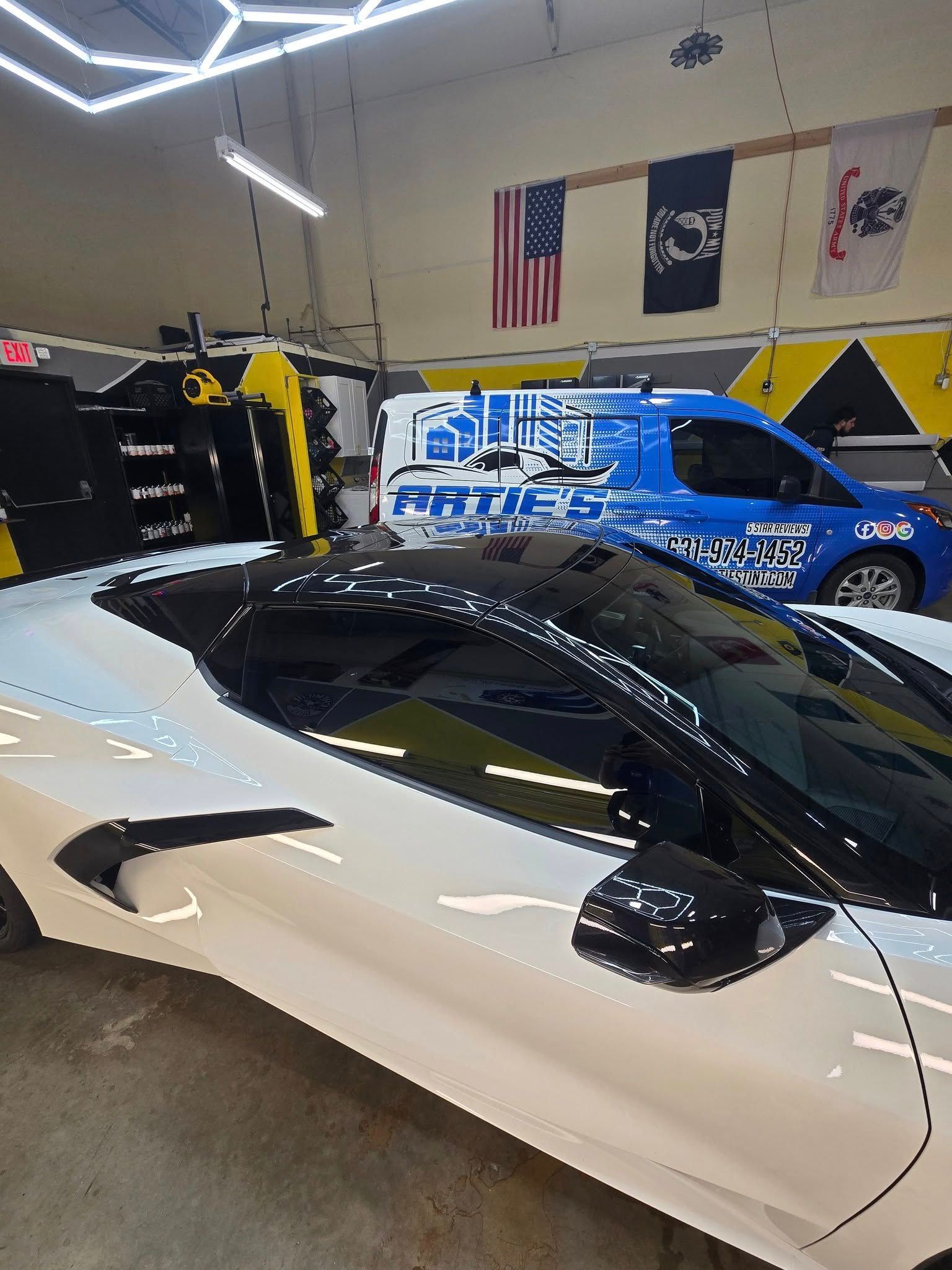 A white sports car is parked in a garage next to a blue van.