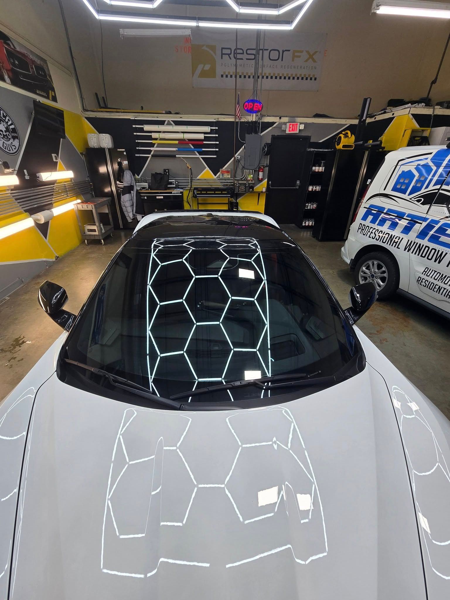 A white car with a honeycomb design on the windshield is parked in a garage.