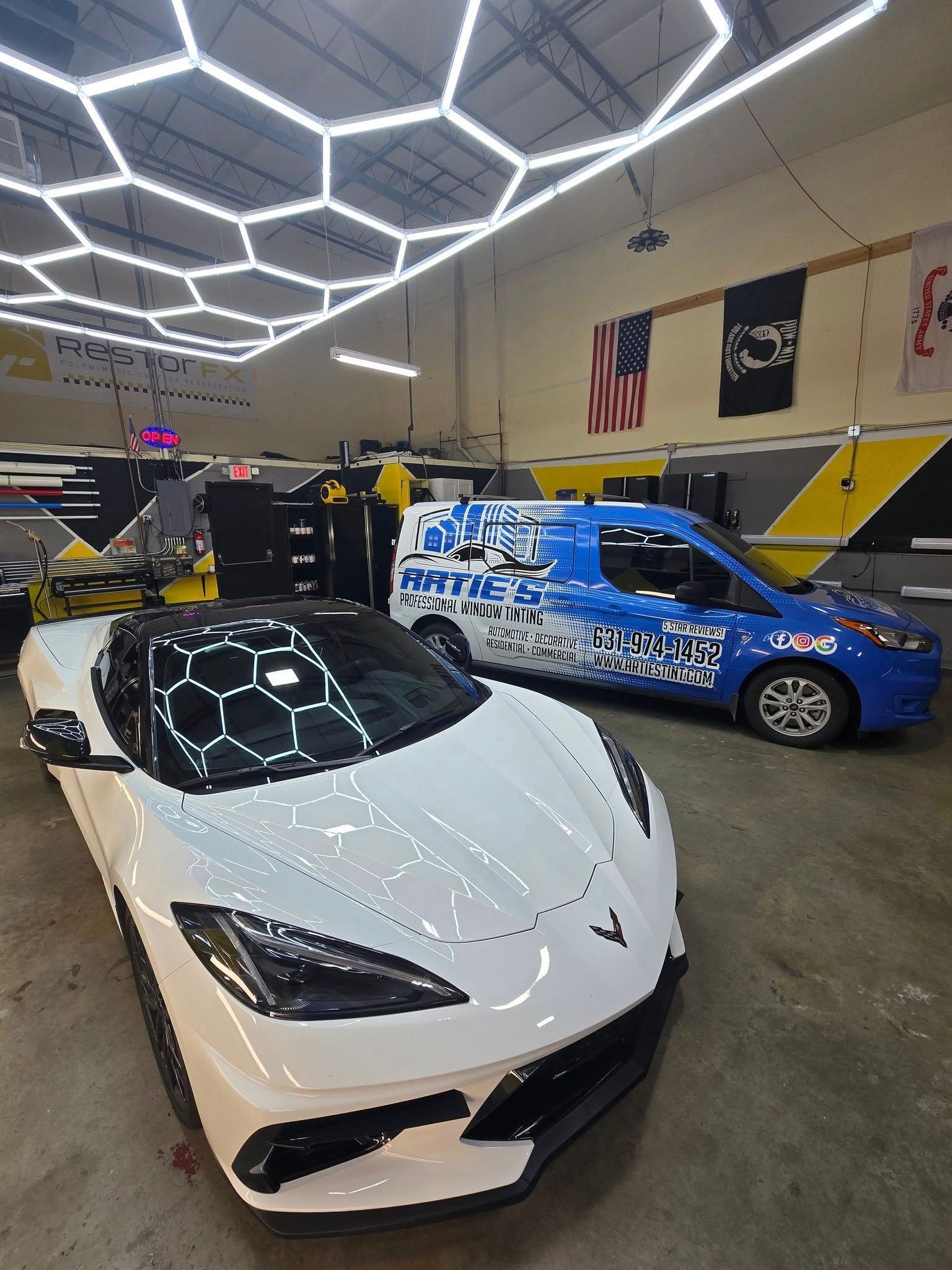 A white sports car is parked next to a blue van in a garage.