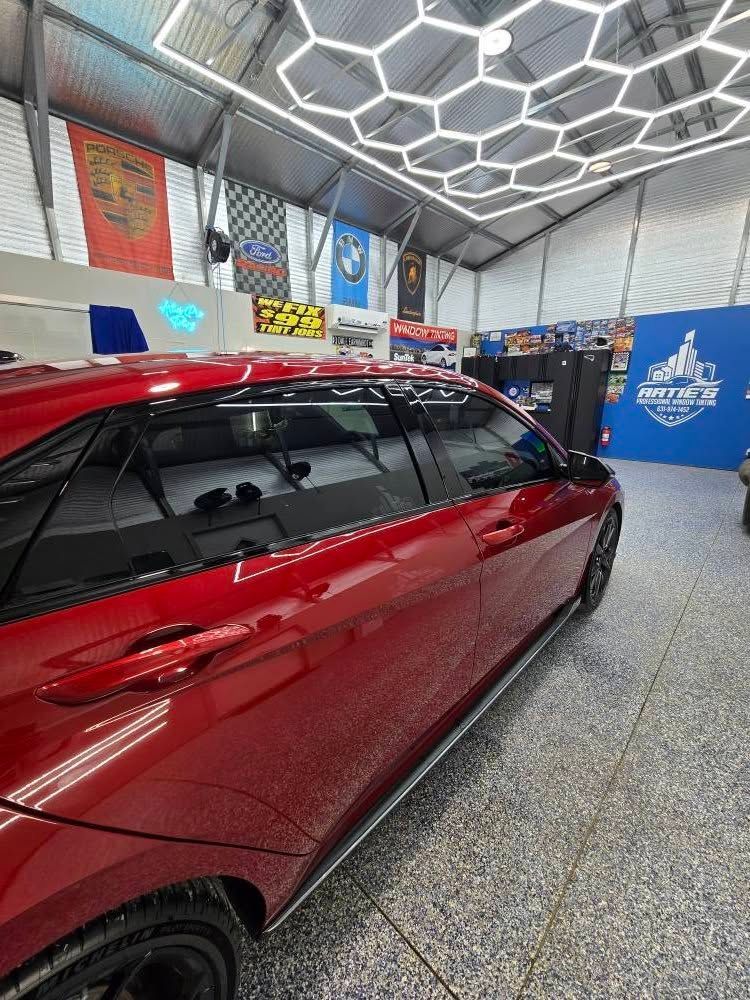 A red car is parked in a garage with a honeycomb ceiling.
