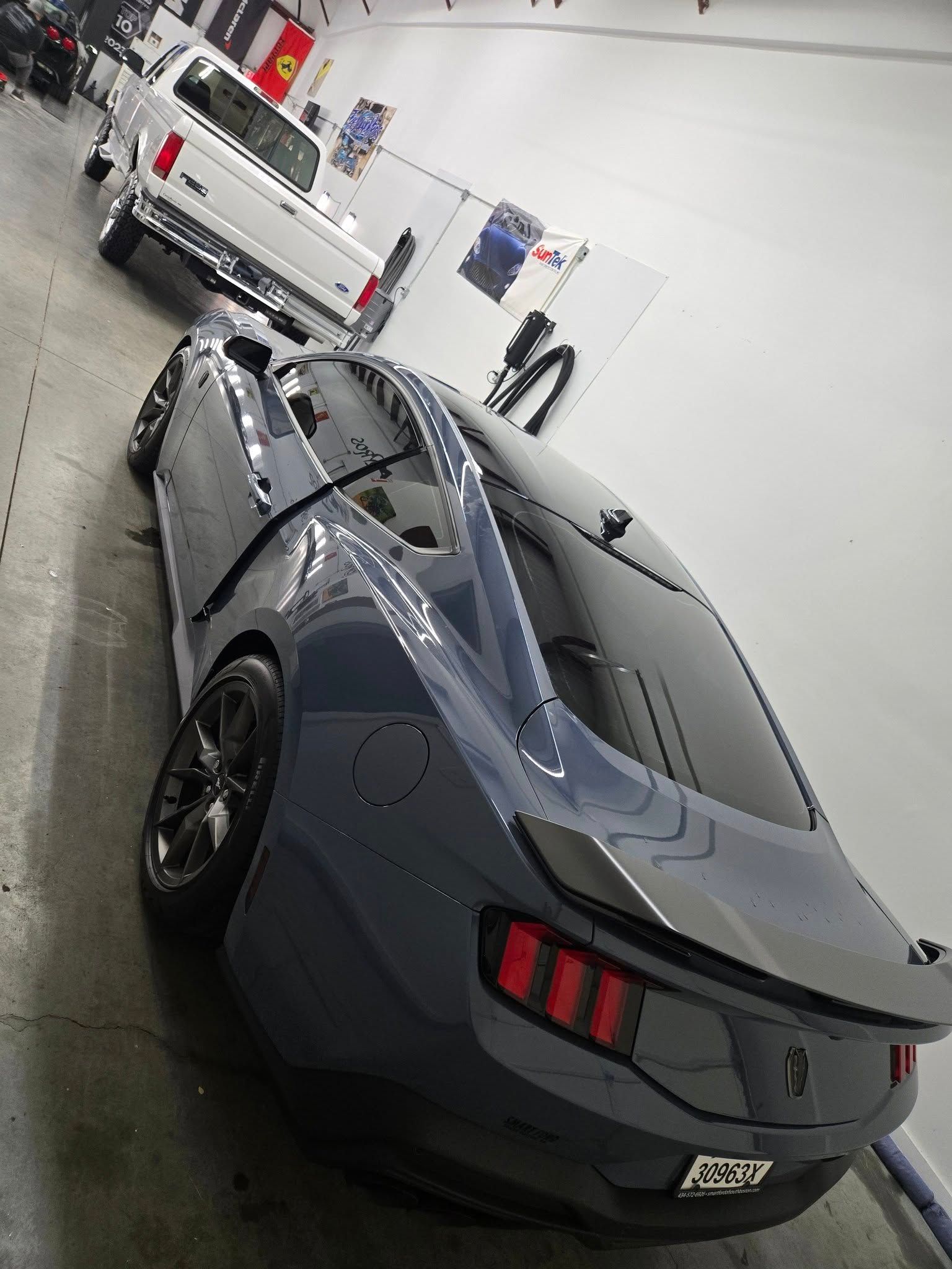 A gray mustang is parked in a garage next to a white truck.