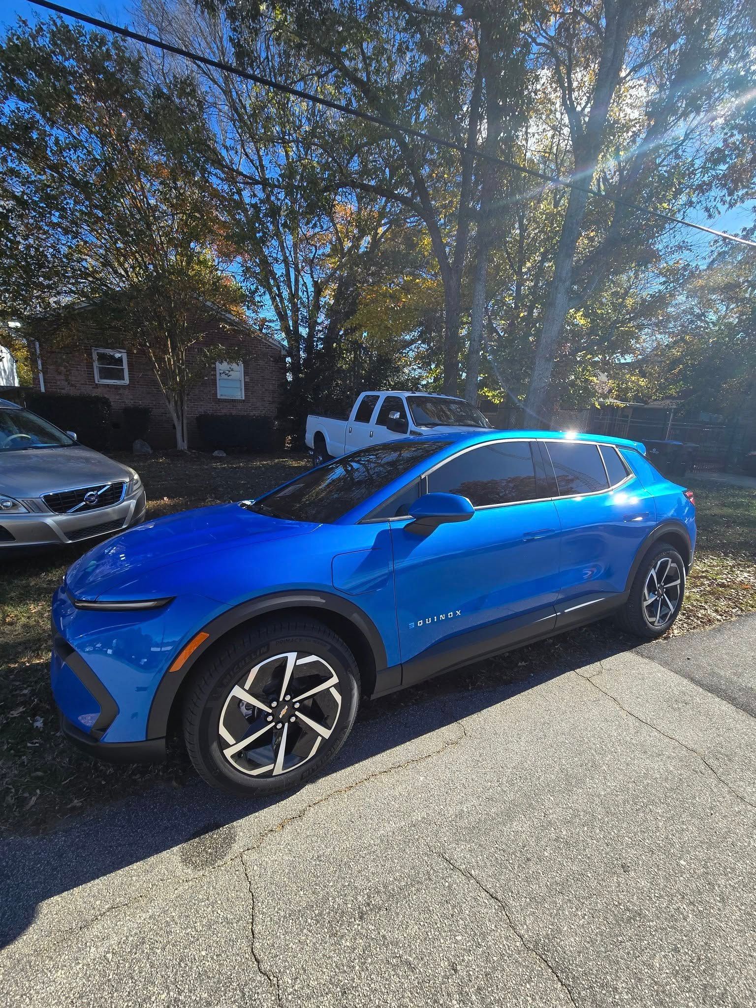 A blue car is parked on the side of the road in front of a house.