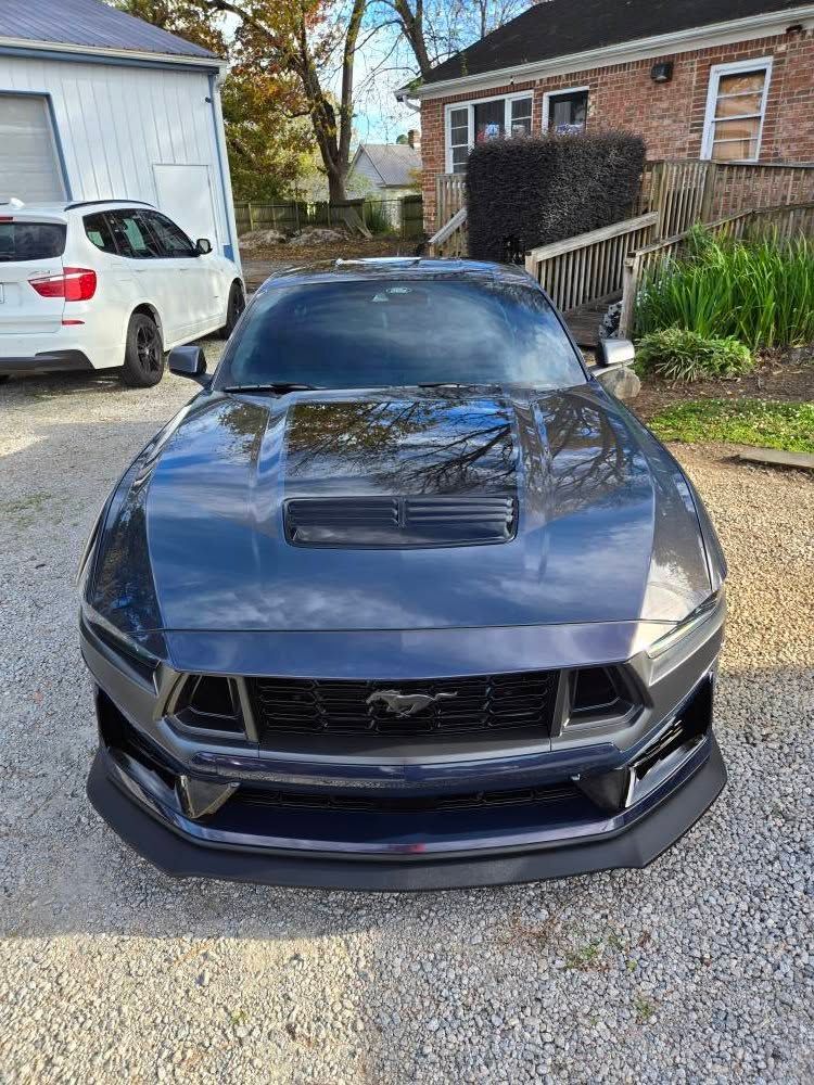 A black mustang is parked in a gravel lot in front of a house.