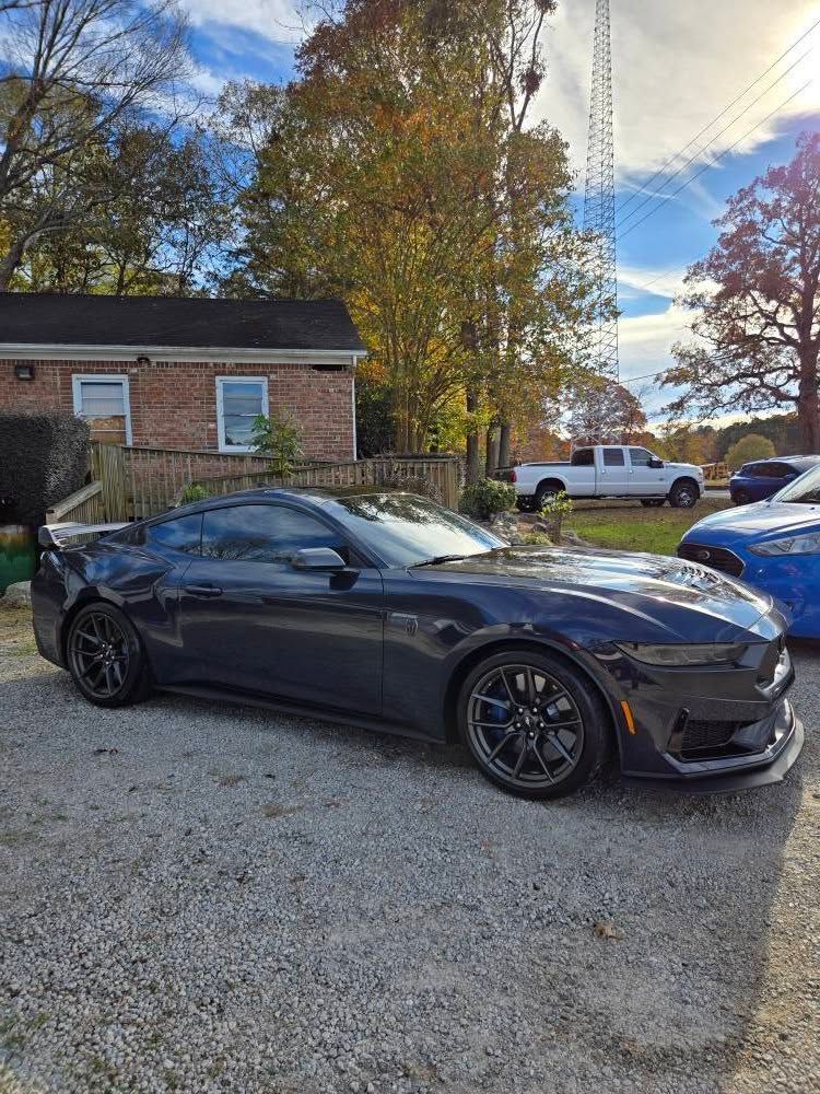 A black mustang is parked in front of a brick house.