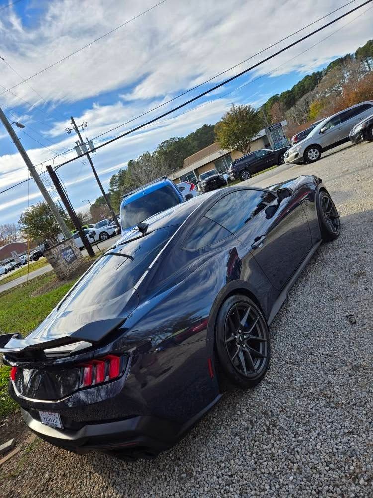 A black mustang is parked in a gravel lot.
