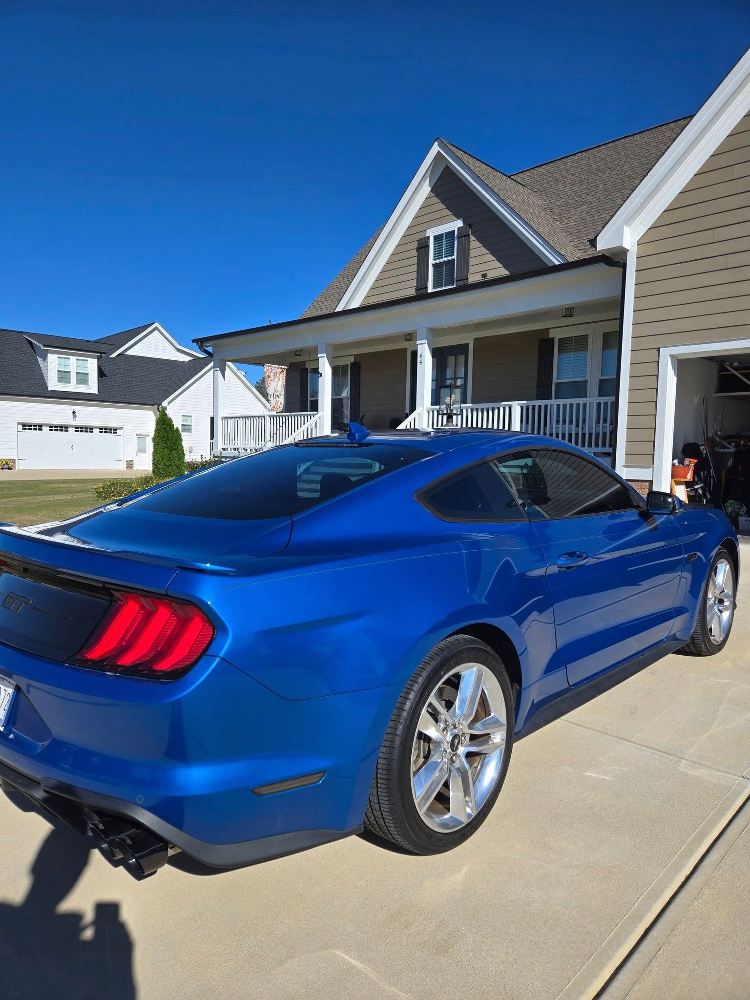 A blue mustang is parked in front of a house in a driveway.
