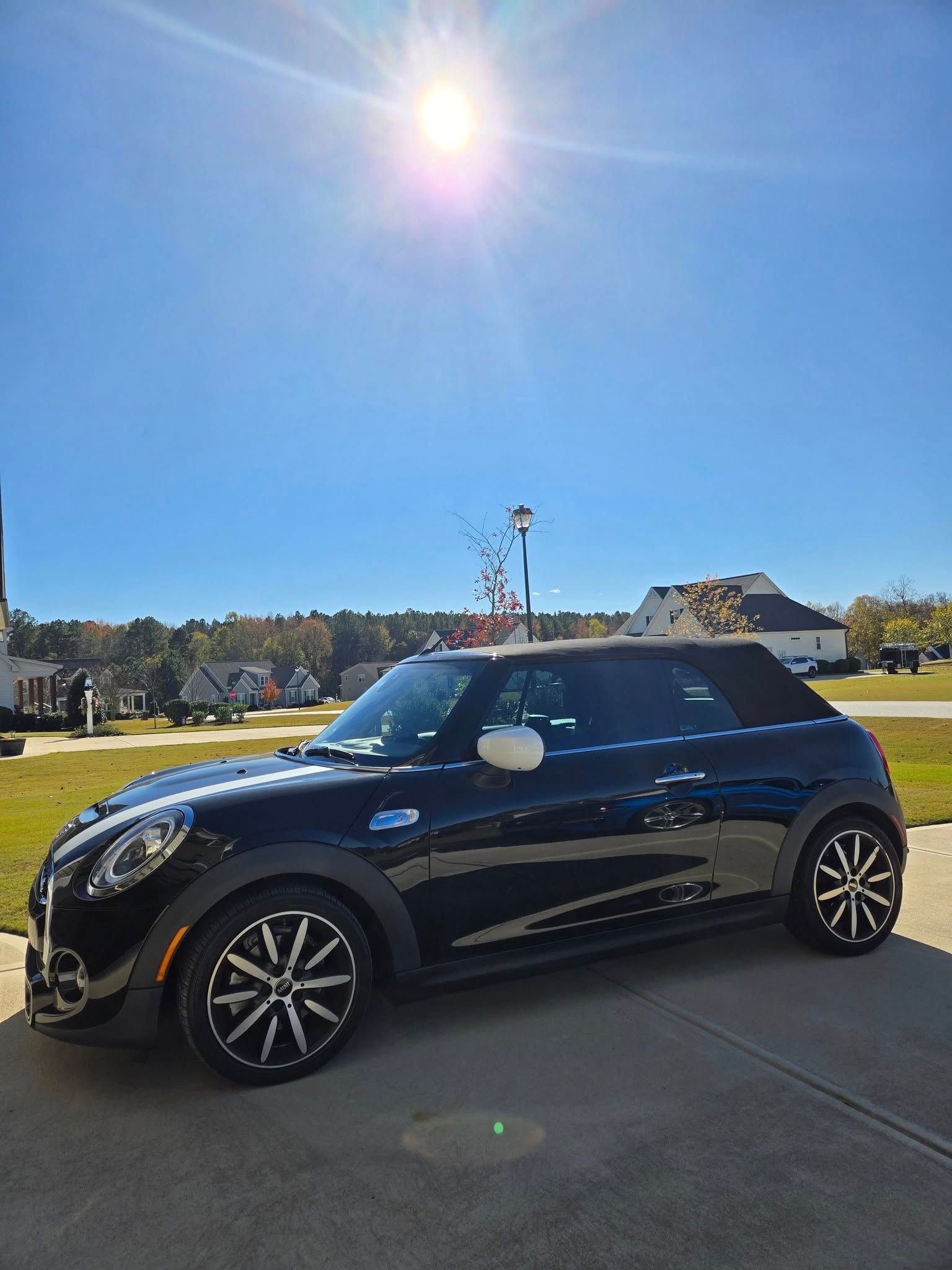 A black mini cooper is parked in a driveway on a sunny day.