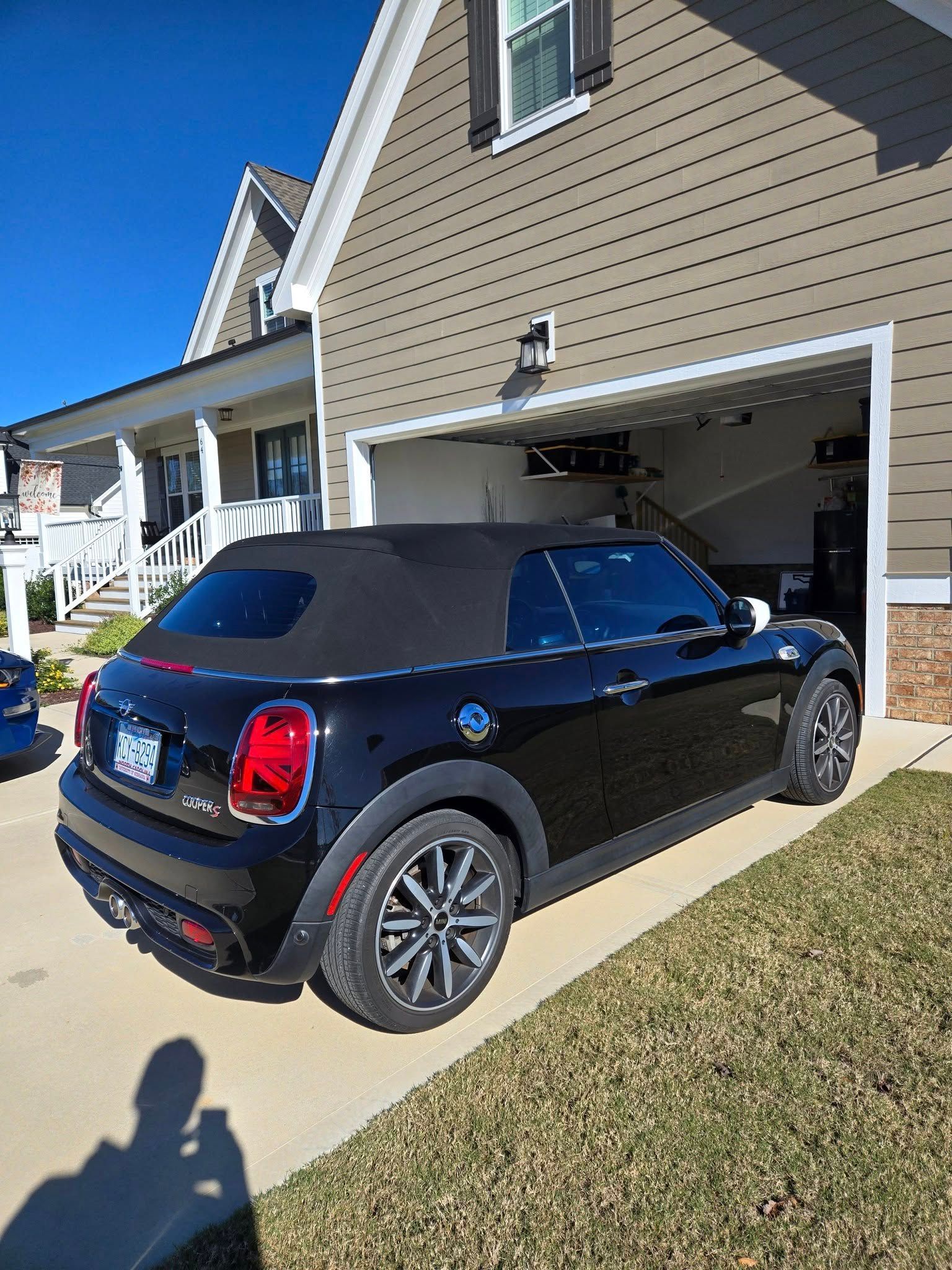 A black mini cooper convertible is parked in front of a house.